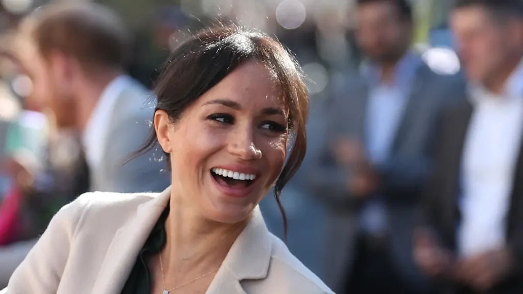 Serial Netflix Terbaru Meghan Markle kembali berkarier, Meghan Markle tersenyum lebar dan tertawa di luar ruangan dengan latar belakang orang-orang yang kabur
