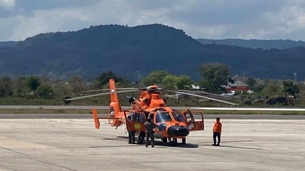 Evakuasi Korban Gempa NTT 7 Warga Luka Resmi Diangkut Helikopter 52 Evakuasi Gempa, Helikopter oranye SAR terparkir di landasan dengan latar belakang perbukitan