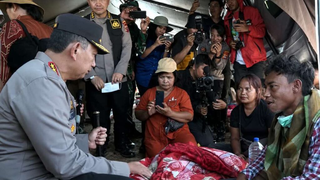 kapolri sigit berseragam berdialog dengan warga di tenda pengungsian, dikelilingi oleh warga dan awak media yang mengambil foto