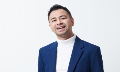 Raffi Ahmad mengenakan blazer biru dan baju putih berkerah tinggi sambil tersenyum