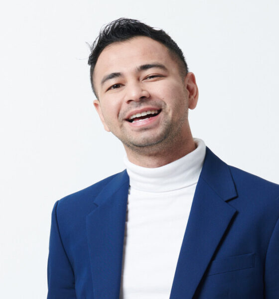 Raffi Ahmad mengenakan blazer biru dan baju putih berkerah tinggi sambil tersenyum