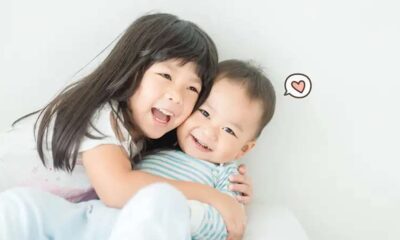 Seorang anak perempuan tersenyum lebar sambil memeluk erat adiknya yang bersorak gembira