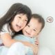 Seorang anak perempuan tersenyum lebar sambil memeluk erat adiknya yang bersorak gembira
