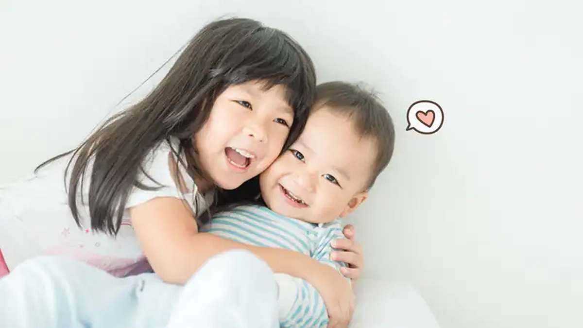 Seorang anak perempuan tersenyum lebar sambil memeluk erat adiknya yang bersorak gembira