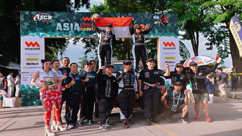 Duet Balap Florist dan Dokter Gigi Resmi Taklukkan AXCR 2026 53 Duet balap komunitas dunia se Asia, Tim balap mobil berpose bersama di depan latar belakang AXCR Asia Cross Country Rally sambil merayakan kemenangan