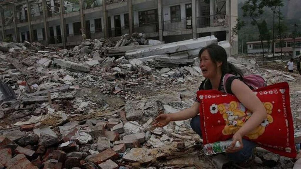 Seorang perempuan menangis di dekat reruntuhan bangunan akibat gempa bumi sambil membawa bantal merah dan botol air