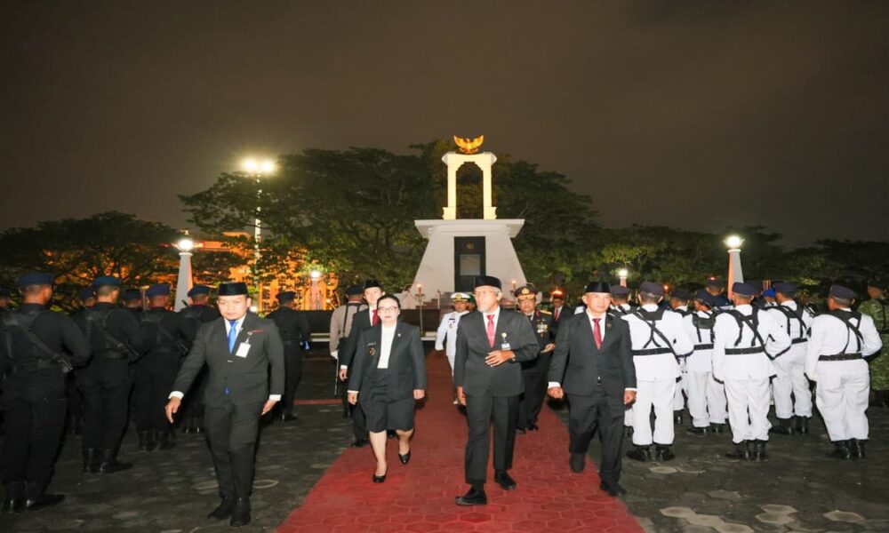 Para pejabat dan pasukan kehormatan berjalan di karpet merah di depan monumen pada malam hari