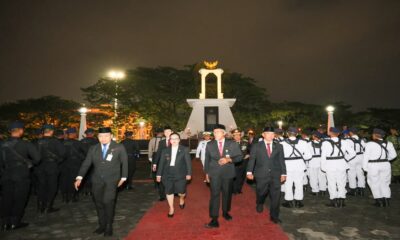 Para pejabat dan pasukan kehormatan berjalan di karpet merah di depan monumen pada malam hari
