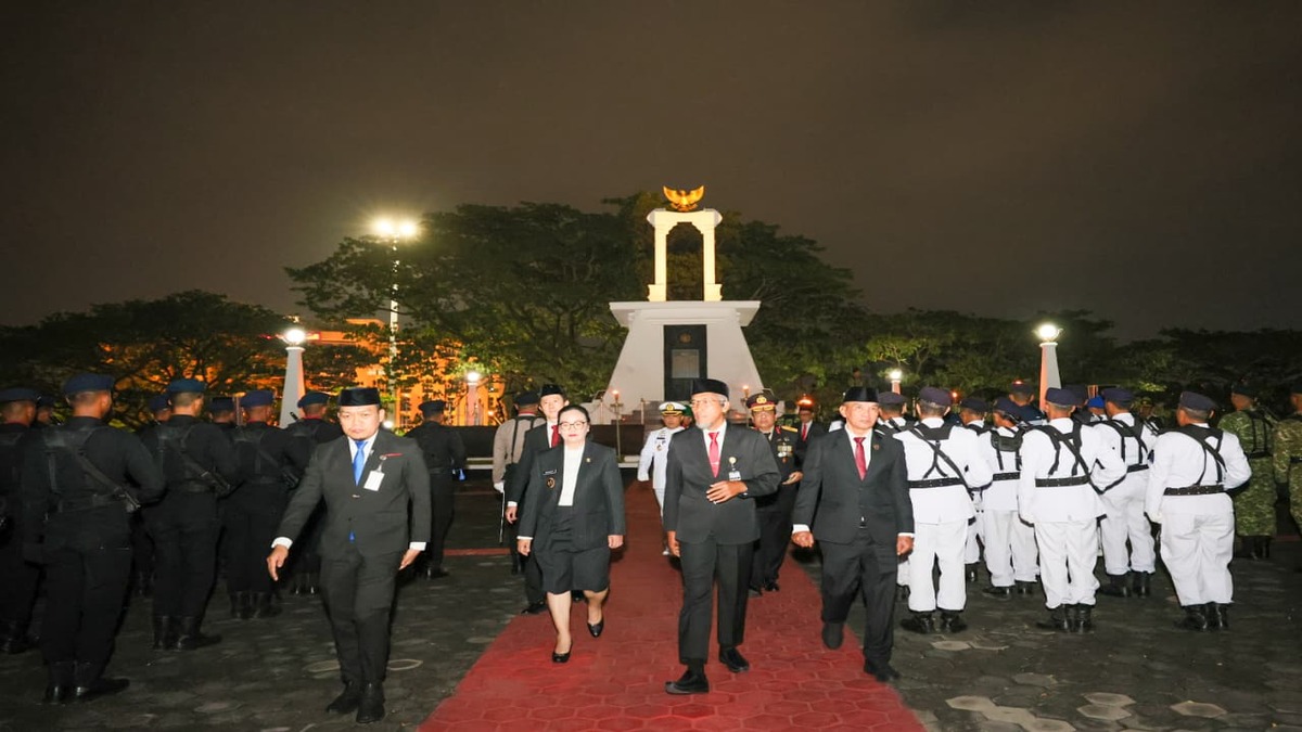 Para pejabat dan pasukan kehormatan berjalan di karpet merah di depan monumen pada malam hari