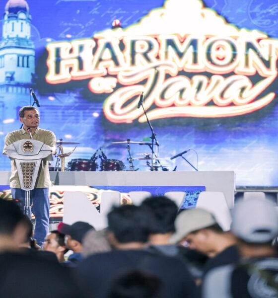 Seorang pria berdiri di atas panggung di depan layar bertuliskan Harmony of Java, berbicara di hadapan penonton yang memadati area