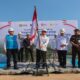 Menteri ESDM memegang tiang bendera Merah Putih dalam acara peluncuran dan peletakan batu pertama PLTS, didampingi pejabat dan aparat keamanan