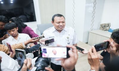 Seorang pria berseragam putih dikelilingi wartawan yang mengarahkan ponsel dan kamera untuk mewawancarainya