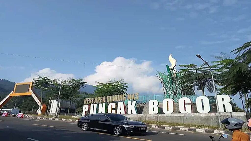 Papan penanda Rest Area Gunung Mas Puncak Bogor di pinggir jalan raya dengan latar langit biru dan awan putih