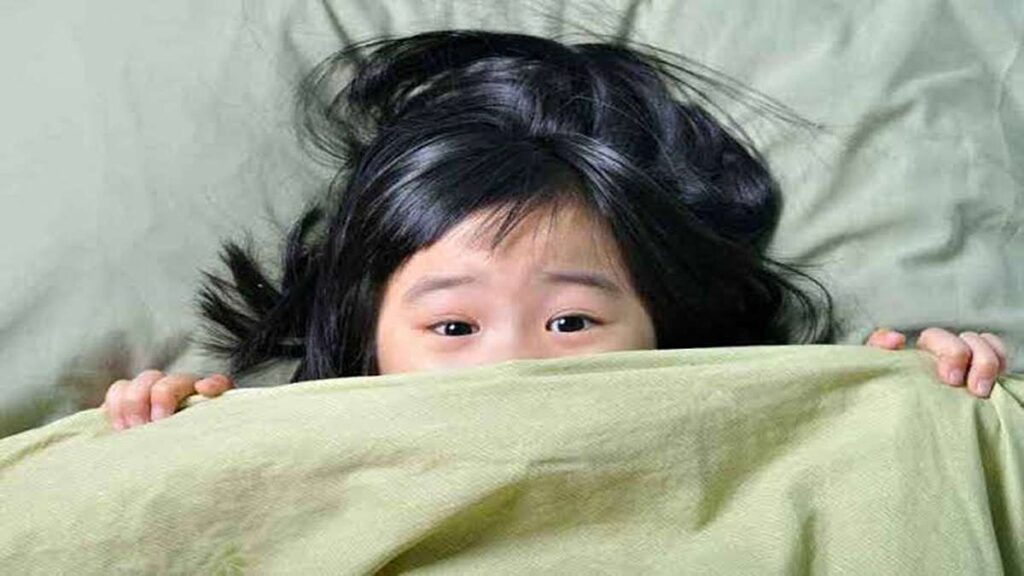 Anak perempuan bersembunyi di balik selimut hijau dengan mata mengintip keluar