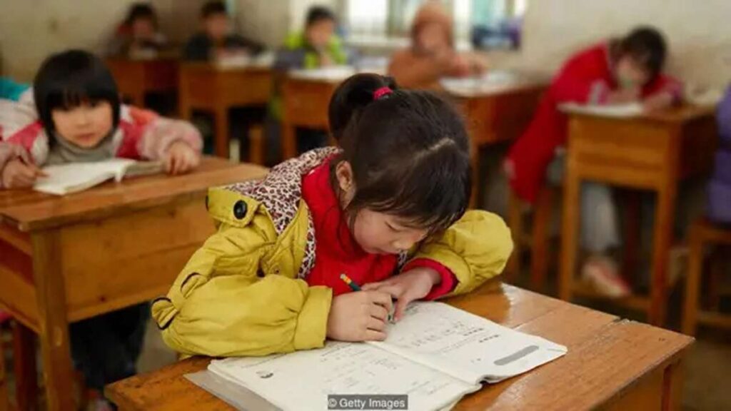 Anak-anak sedang belajar di dalam kelas di balik meja kayu
