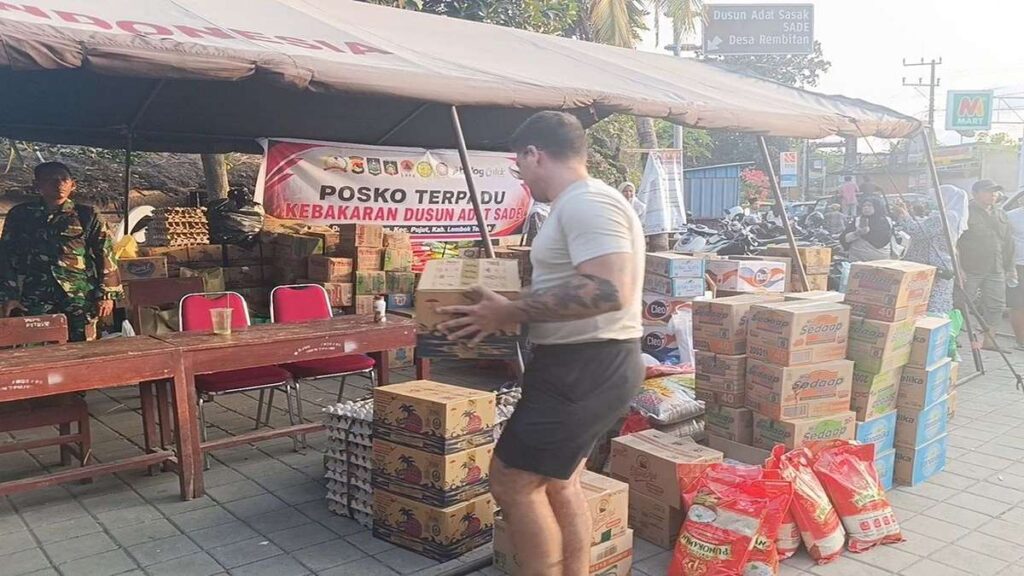 Seorang pria membawa kardus bantuan di depan posko terpadu kebakaran Dusun Adat Sade