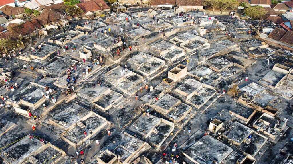 Foto udara pemukiman padat yang rata dengan tanah dan hangus terbakar, dikelilingi warga yang memeriksa reruntuhan