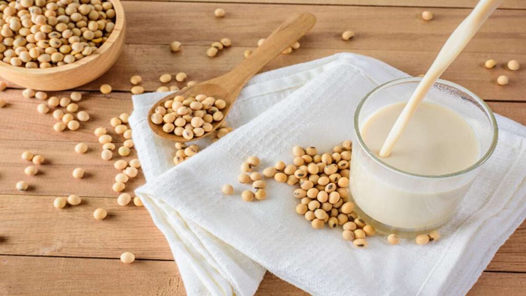 Perbandingan Jumlah Protein Berbagai Jenis Susu dari Almond hingga Susu Sapi 53 Segelas susu kedelai dengan biji kedelai mentah di atas meja kayu