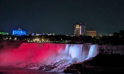Air terjun Niagara pada malam hari diterangi cahaya merah dan putih di bawah langit malam dengan latar belakang gedung-gedung kota yang bercahaya