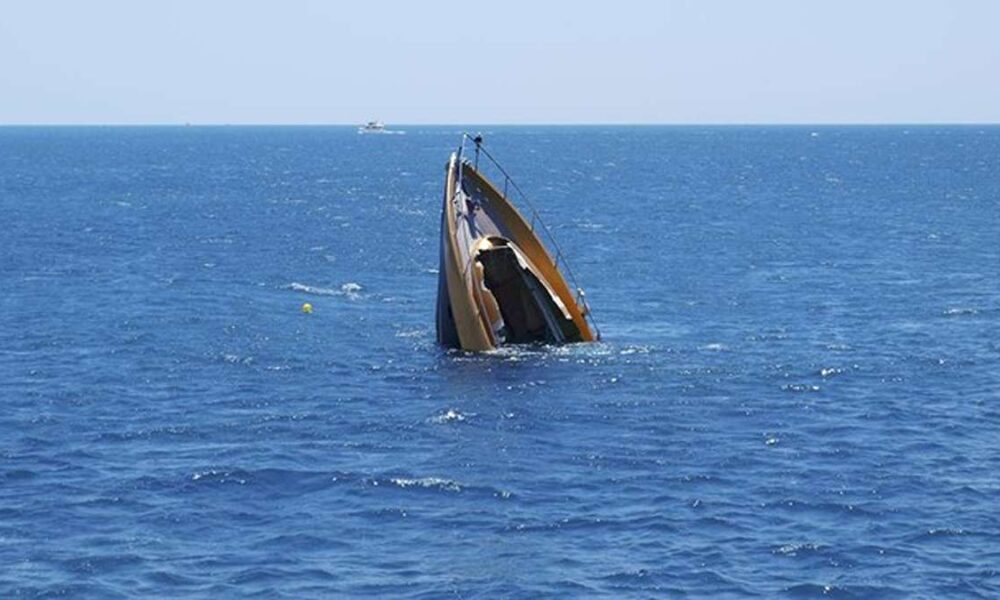 Kecelakaan Kapal Feri di Zimbabwe Sebuah kapal pesiar tenggelam secara vertikal di tengah laut yang biru, dengan bagian haluan mengarah ke atas