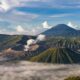 Pemandangan lanskap Gunung Bromo berselimut kabut dengan latar pegunungan dan langit berawan