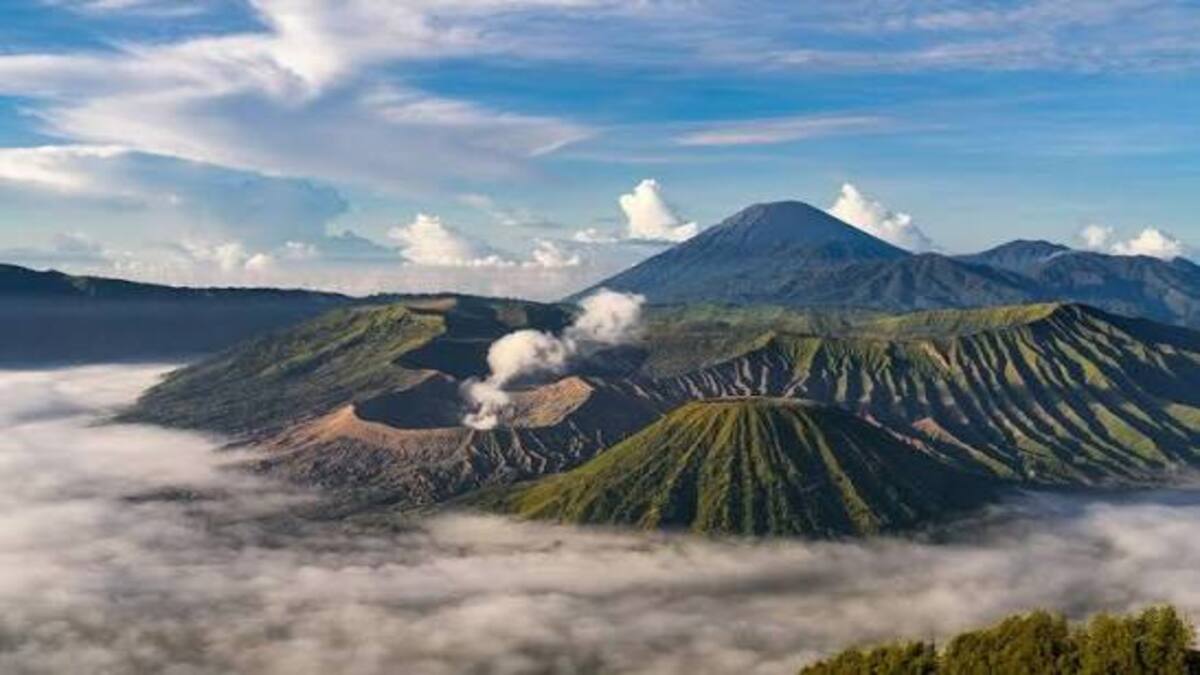 Pemandangan lanskap Gunung Bromo berselimut kabut dengan latar pegunungan dan langit berawan