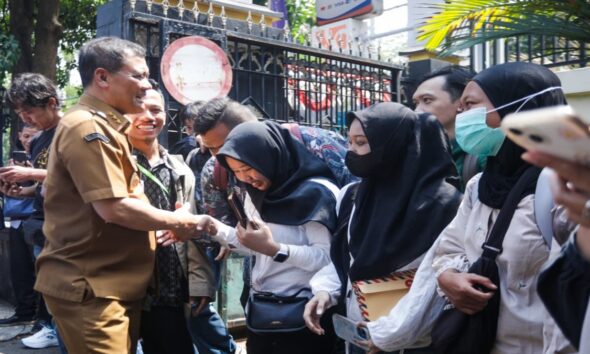 Seorang pejabat berseragam khaki menyalami warga di antara kerumunan