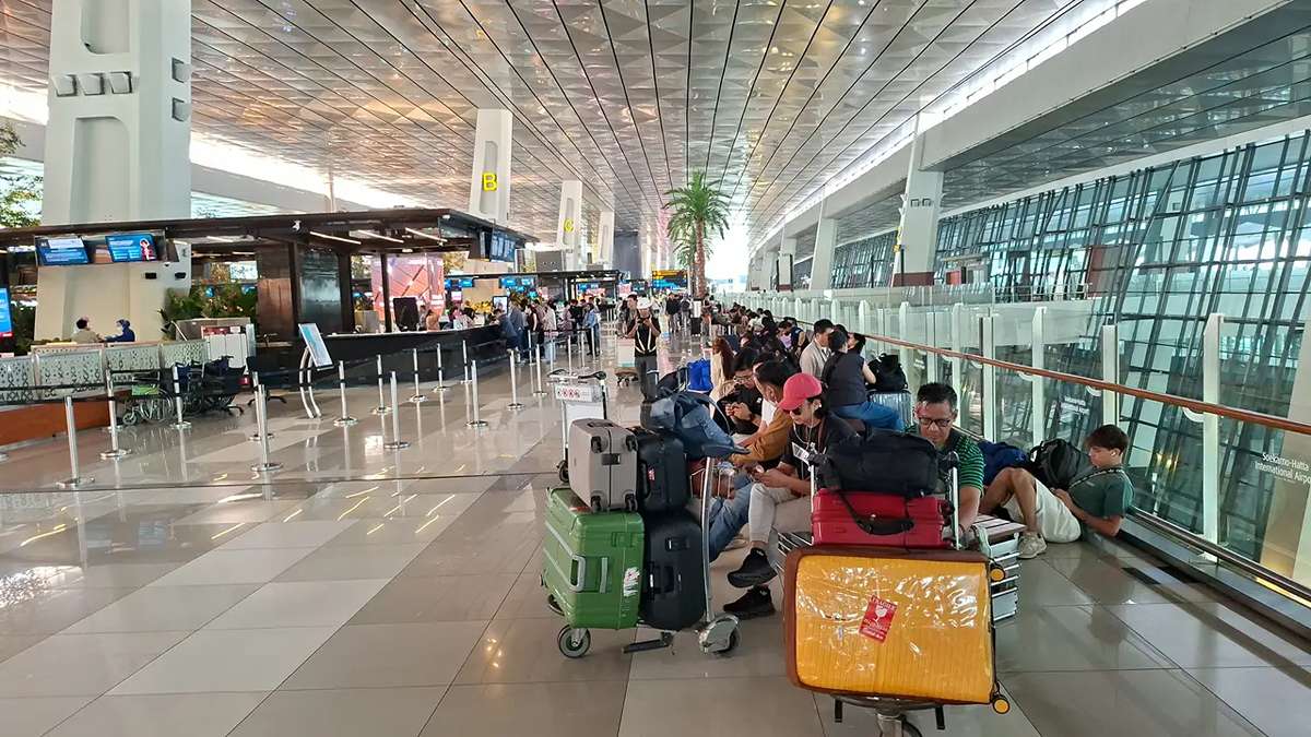Suasana terminal bandara dengan calon penumpang yang duduk menunggu di samping koper-koper mereka