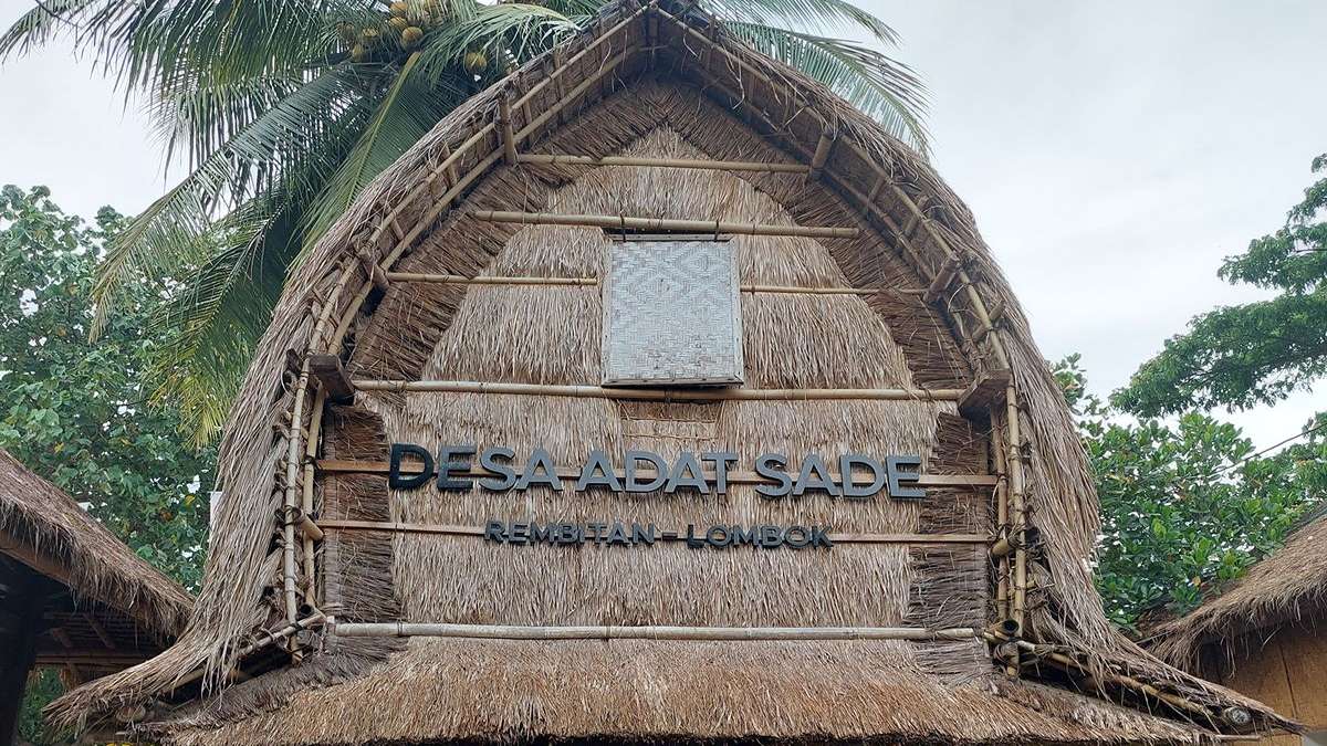 Salah 1 Museum Sade Ditargetkan Tuntas Sebelum MotoGP Mandalika 52 Warga berdiri di antara puing-puing bangunan dan pohon-pohon yang hangus terbakar setelah kerusuhanSalah 1 Museum Sade Ditargetkan Tuntas Sebelum MotoGP Mandalika, Tampak depan rumah tradisional Sasak dengan atap jerami dan tulisan Desa Adat Sade Rembitan Lombok di dindingnya
