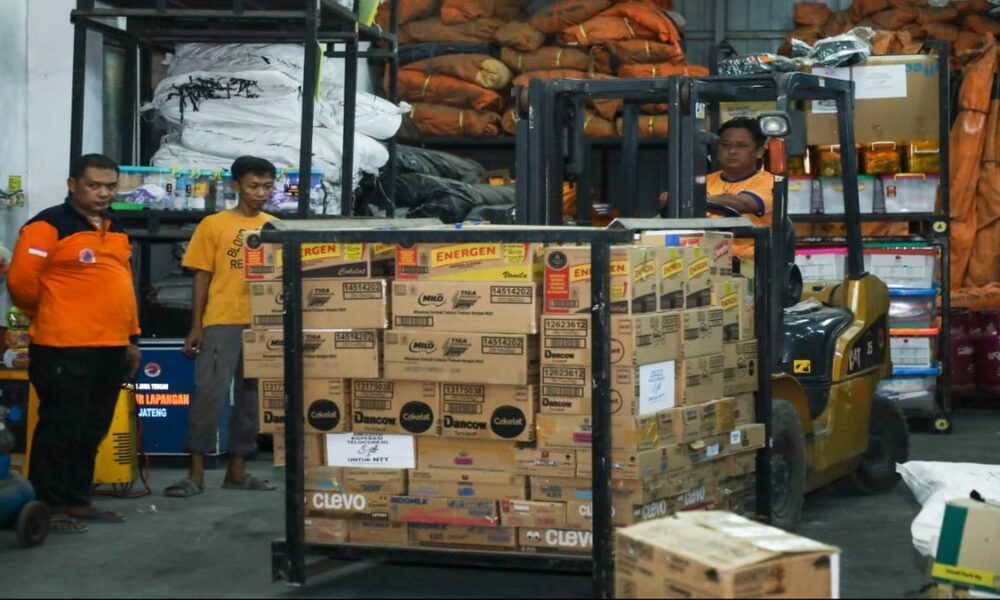 Petugas gudang menyiapkan kardus bantuan logistik dengan menggunakan forklift di dalam gudang