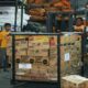 Petugas gudang menyiapkan kardus bantuan logistik dengan menggunakan forklift di dalam gudang