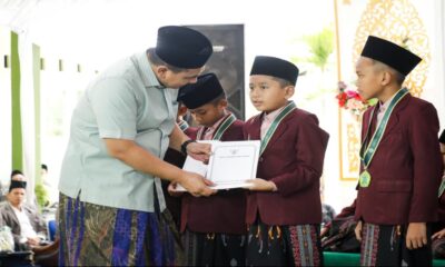 Seorang pria mengenakan peci dan sarung menyerahkan sertifikat kepada santri berseragam jas merah marun dan peci hitam
