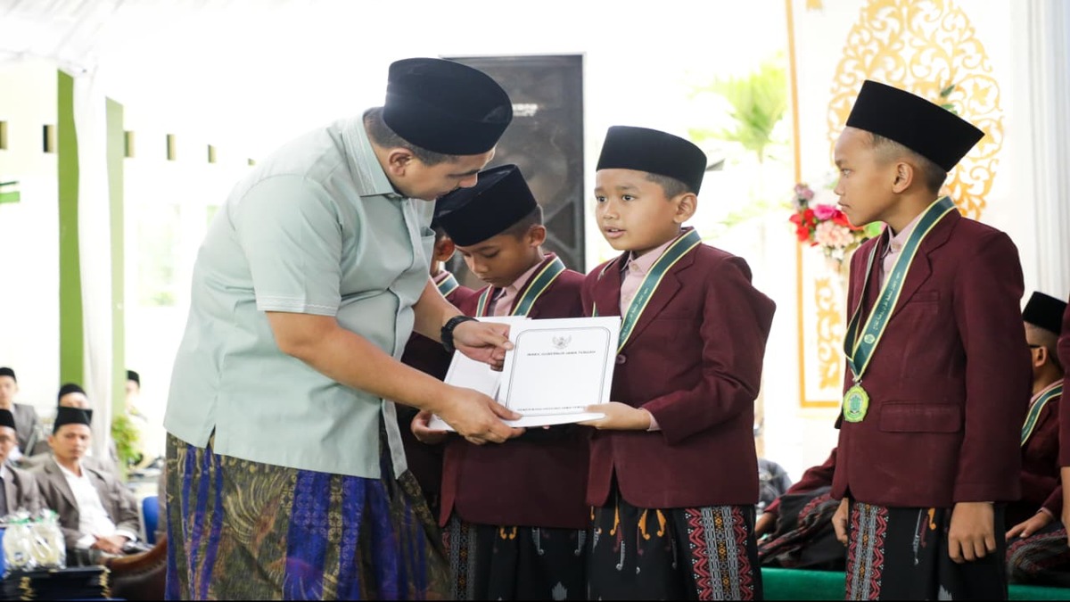 Seorang pria mengenakan peci dan sarung menyerahkan sertifikat kepada santri berseragam jas merah marun dan peci hitam