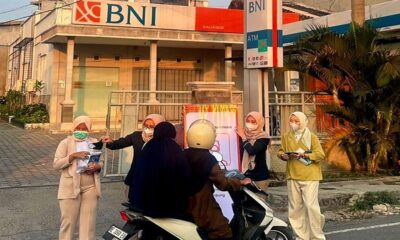 Beberapa wanita bermasker membagikan brosur kepada pengendara motor di depan gedung bank BNI