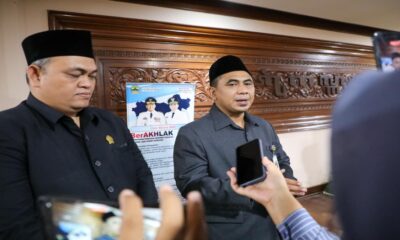 Dua orang pria berpeci hitam mengenakan pakaian resmi sedang memberikan keterangan kepada wartawan