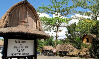 Warga berdiri di antara puing-puing bangunan dan pohon-pohon yang hangus terbakar setelah kerusuhanSalah 1 Museum Sade Ditargetkan Tuntas Sebelum MotoGP Mandalika, Gapura selamat datang di Desa Adat Sasak Sade Rembitan Lombok dengan bangunan beratap jerami di latar belakang