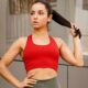 7 Rahasia Ampuh Cara Menata Rambut Agar Tidak Lepek dan Bau Setelah Olahraga 52 Seorang wanita berambut gelap memakai sport bra merah dan memegang rambutnya, berpose di luar ruangan dengan latar dinding modern