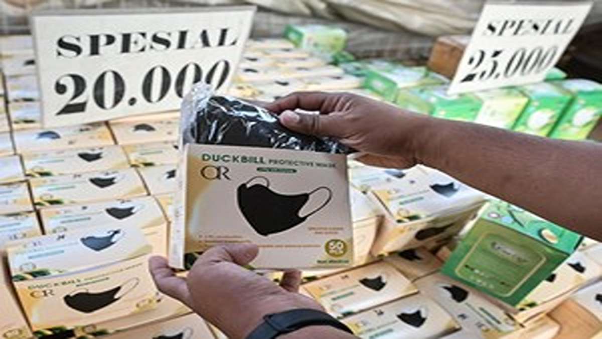 Wajib Tahu! Cara Alternatif Lindungi Diri dari Abu Vulkanik Saat Masker Langka 53 Seseorang menunjukkan kotak masker wajah duckbill berwarna hitam dengan latar belakang tumpukan kotak masker dan label harga
