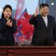 Putri Kim Jong Un, Berusia 13 Tahun Dipersiapkan Jadi Penerus, Kim Jong Un dan putrinya melambaikan tangan kepada orang banyak di depan latar belakang bendera merah di Korea Utara