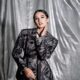 Maudy Ayunda mengenakan blazer bermotif abu-abu dengan latar belakang tirai perak berkilau