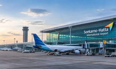 Pesawat komersial parkir di terminal Bandara Internasional Soekarno-Hatta dengan latar menara pengawas