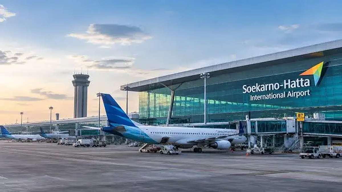 Pesawat komersial parkir di terminal Bandara Internasional Soekarno-Hatta dengan latar menara pengawas