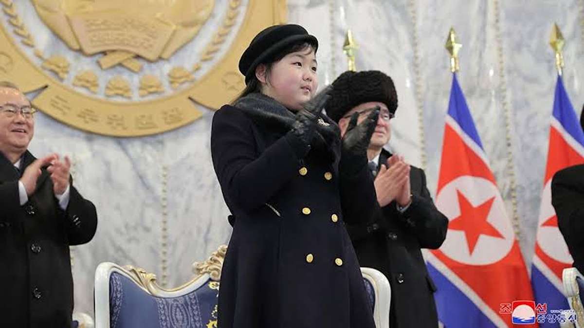 Putri Kim Jong Un, Berusia 13 Tahun Dipersiapkan Jadi Penerus, Ju Ae, putri Kim Jong Un, mengenakan mantel hitam dan topi sedang bertepuk tangan di depan bendera Korea Utara