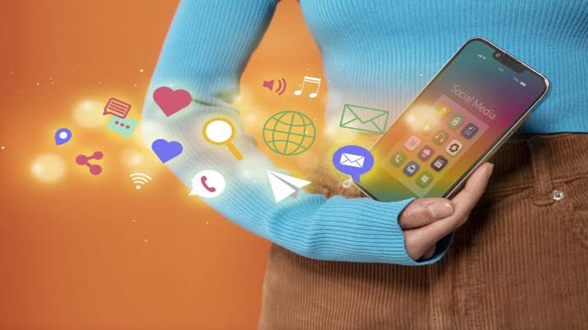 Siap Total! Dukungan Digital MTQ Nasional Jateng Perkuat Akses Informasi 51 Seseorang memegang ponsel dengan berbagai ikon media sosial melayang keluar dari layarnya