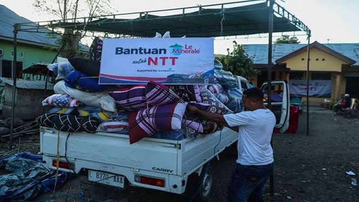 Seorang pria menurunkan bantuan berupa selimut dan kasur dari bak mobil pikap yang membawa spanduk bertuliskan Bantuan untuk NTT