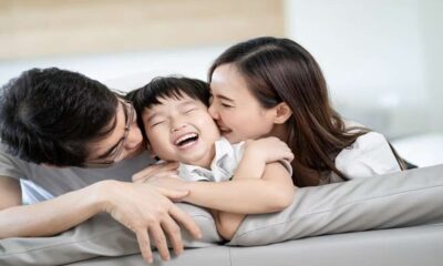 Seorang anak tertawa ceria saat dipeluk dan dicium oleh ayah dan ibunya di sofa