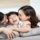 Seorang anak tertawa ceria saat dipeluk dan dicium oleh ayah dan ibunya di sofa