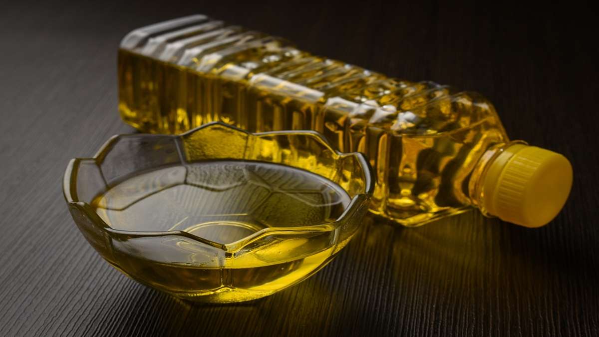Sebotol minyak goreng jernih berwarna kuning di samping mangkuk kecil berisi minyak di atas meja gelap