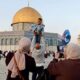 Seorang pria mengangkat anak laki-lakinya di kompleks Masjid Al-Aqsa dengan Kubah Shakhrah di latar belakang