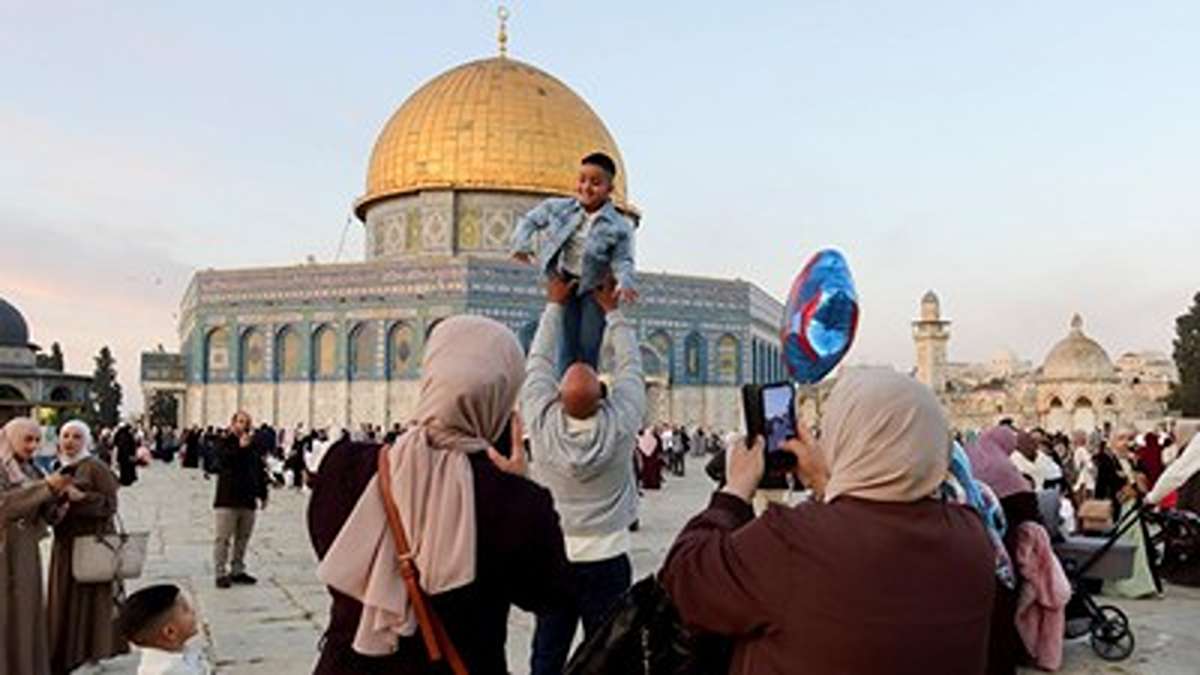 Seorang pria mengangkat anak laki-lakinya di kompleks Masjid Al-Aqsa dengan Kubah Shakhrah di latar belakang